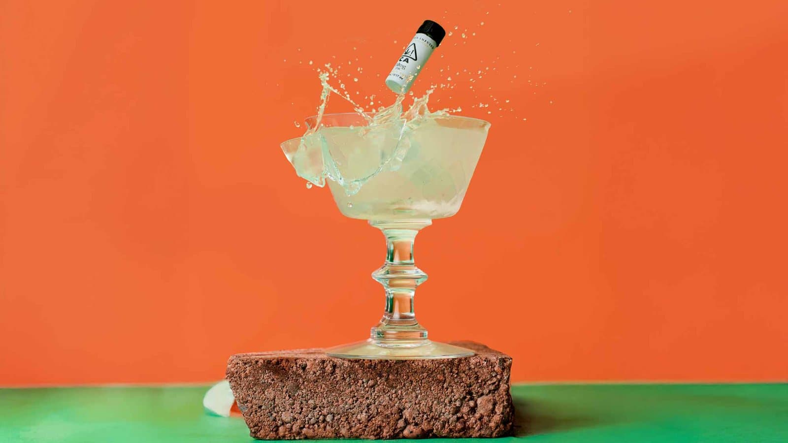 Coupe glass mid-splash on a brick against an orange wall